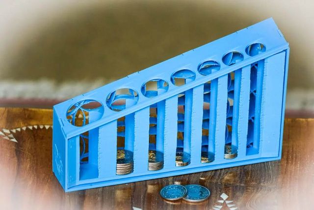 Mechanical coin sorter on a table, with a ramp at the top and a small-to-large series of slots