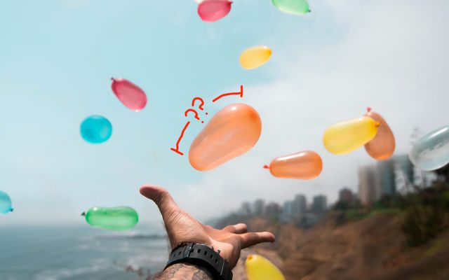 A hand throwing multicolored water balloons in the air
