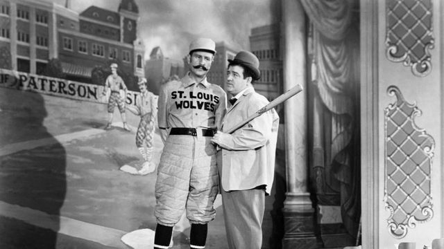 Abbot and Costello
wearing baseball uniforms
under a sign that asks
who's on first
