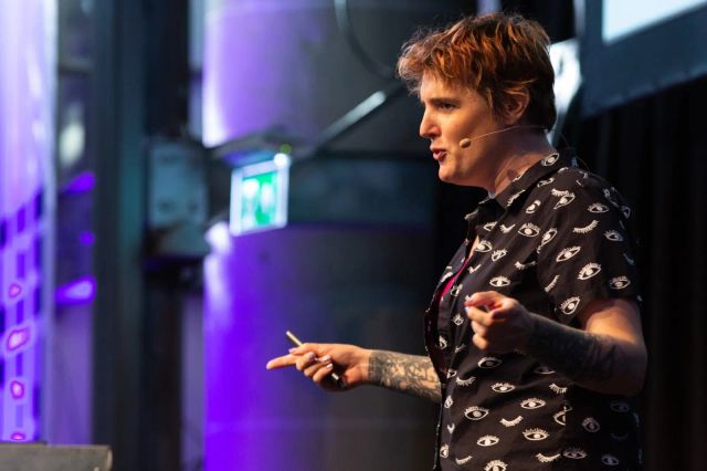 Miriam gesturing on stage, in a black and white shirt covered in eyes